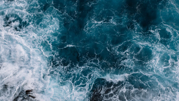 aerial view of white ocean waves against a blue water background