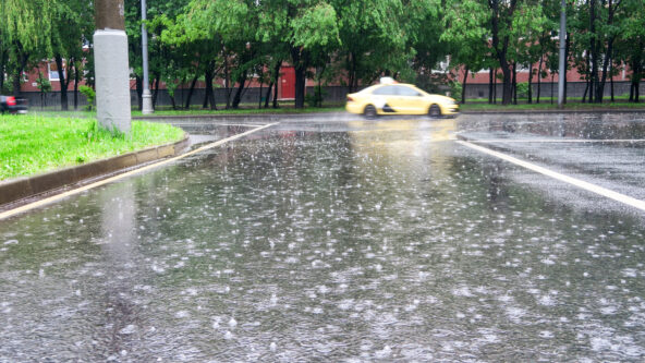 photo precipitation or rain falling on city street with park and taxi cab in the background