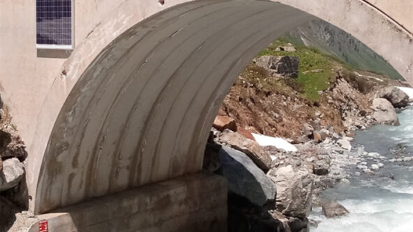 photo RQ-30 mounted on a bridge over a river; non-contact radar sensor takes discharge measurements and keeps public works workers safe. bottom of photo shows a red staff gauge to measure water level