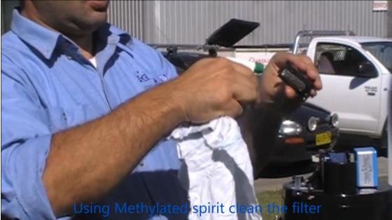 photo from video on tipping bucket rain gauge maintenance; hydrology technician sprays the siphon with isopropyl alcohol or methylated spirit to clean the filter