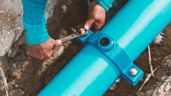 photo of man's hands as worker uses a wrench to secure a bolt on a ground water pipe