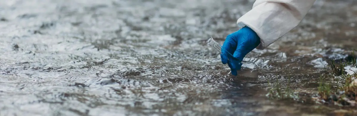 photo of a hand wearing a glove to collect a storm water quality sample in a glass