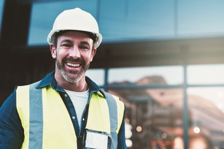 hero photo of public works worker: smiling man wearing a white hard hat, yellow vest work shirt and badge